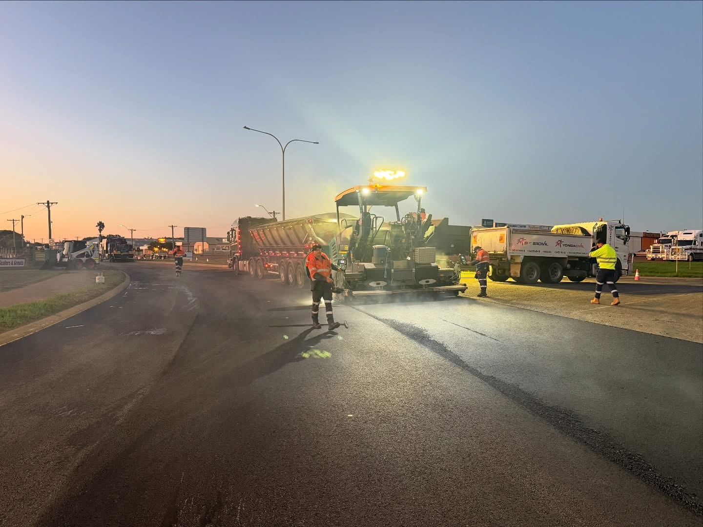 YongaCivil asphalt paver and crew laying fresh asphalt on a Western Australian road at dusk