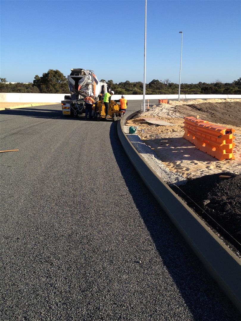 YongaCivil concrete kerbing machine and crew laying continuous kerbing along a freshly sealed road curve