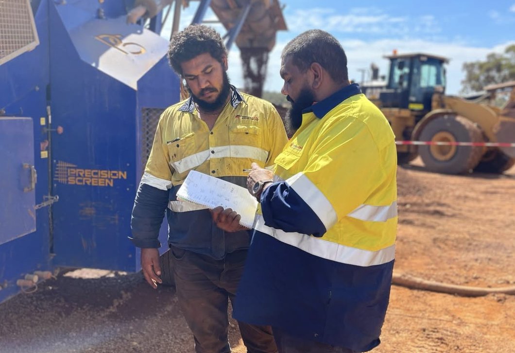 Two YongaCivil workers in hi-vis reviewing notes beside a screening plant with a wheel loader behind